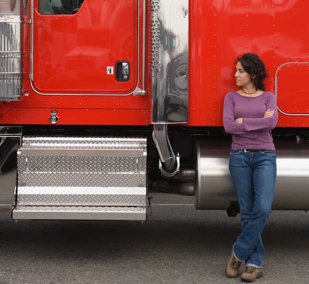 A driver stands near the cab of her truck.