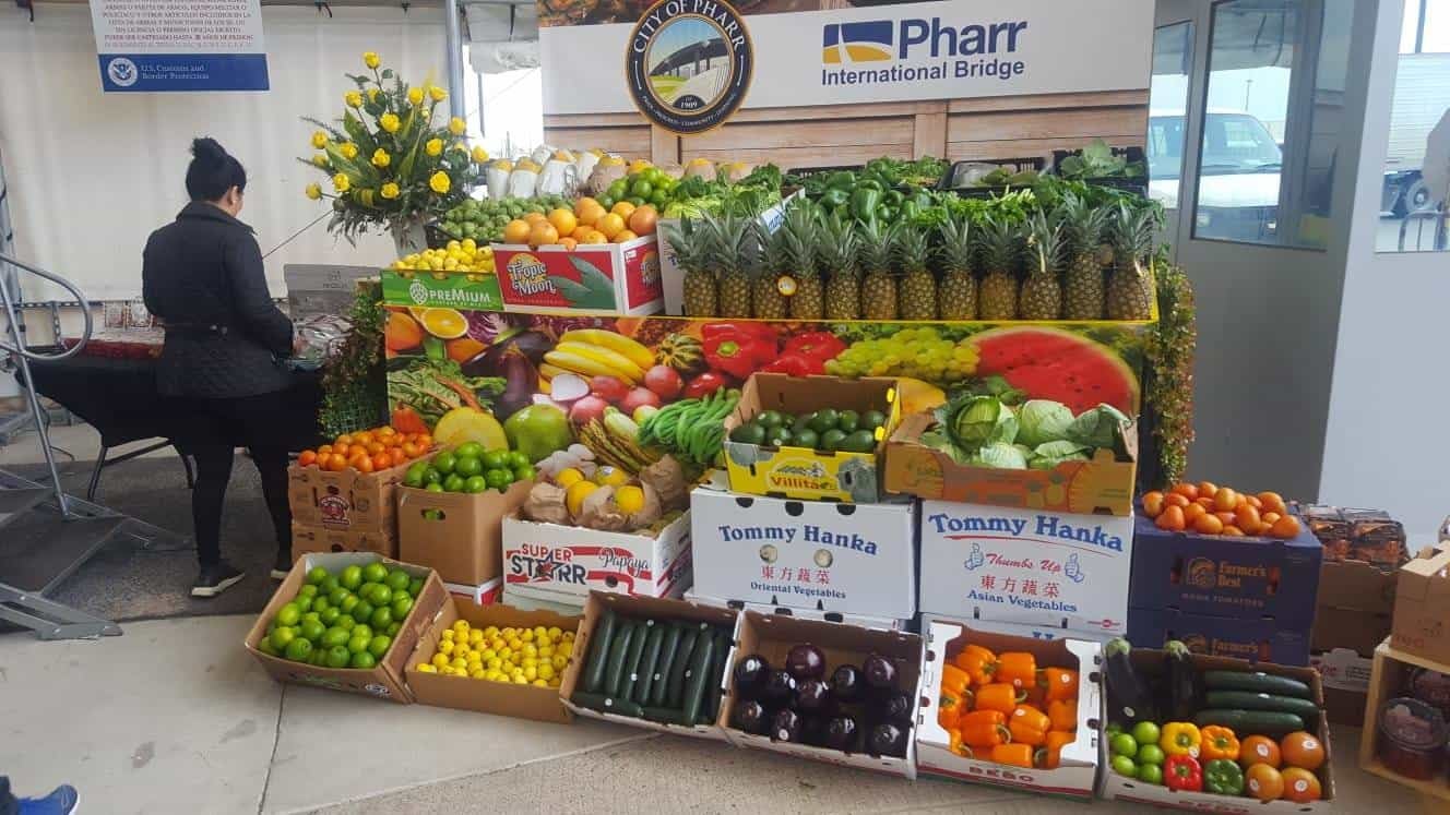 Boxes of produce are displayed in front of a sign that reads Pharr International Bridge.