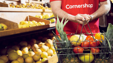Cornershop worker holds basket of fresh fruits and vegetables in the produce section of a grocery store.