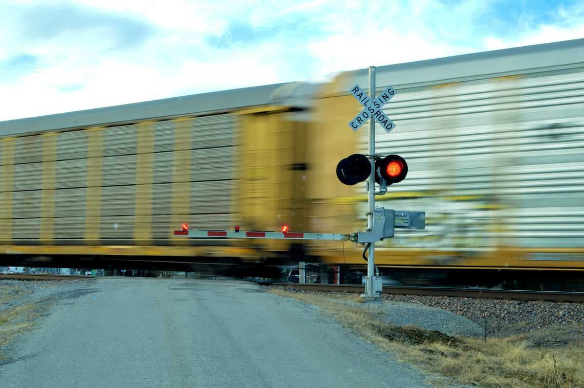 A photograph of railcars passing through a railroad crossing. A railroad crossing sign is in front of the railcars and is signaling that the intersection can't be crossed by vehicular traffic.