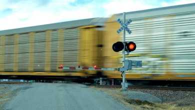 A photograph of railcars passing through a railroad crossing. A railroad crossing sign is in front of the railcars and is signaling that the intersection can't be crossed by vehicular traffic.