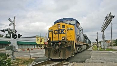 A photograph of a train passing a rail crossing.