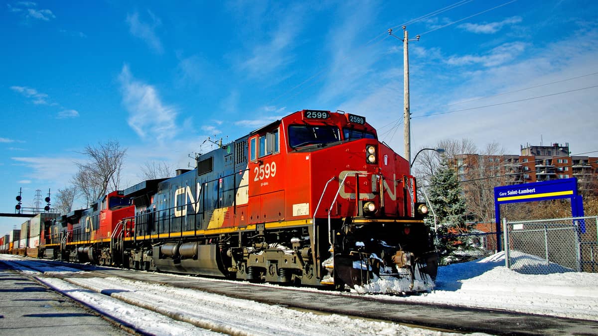 A photograph of a train on a railway track. There is snow on the ground and an apartment building in the background.