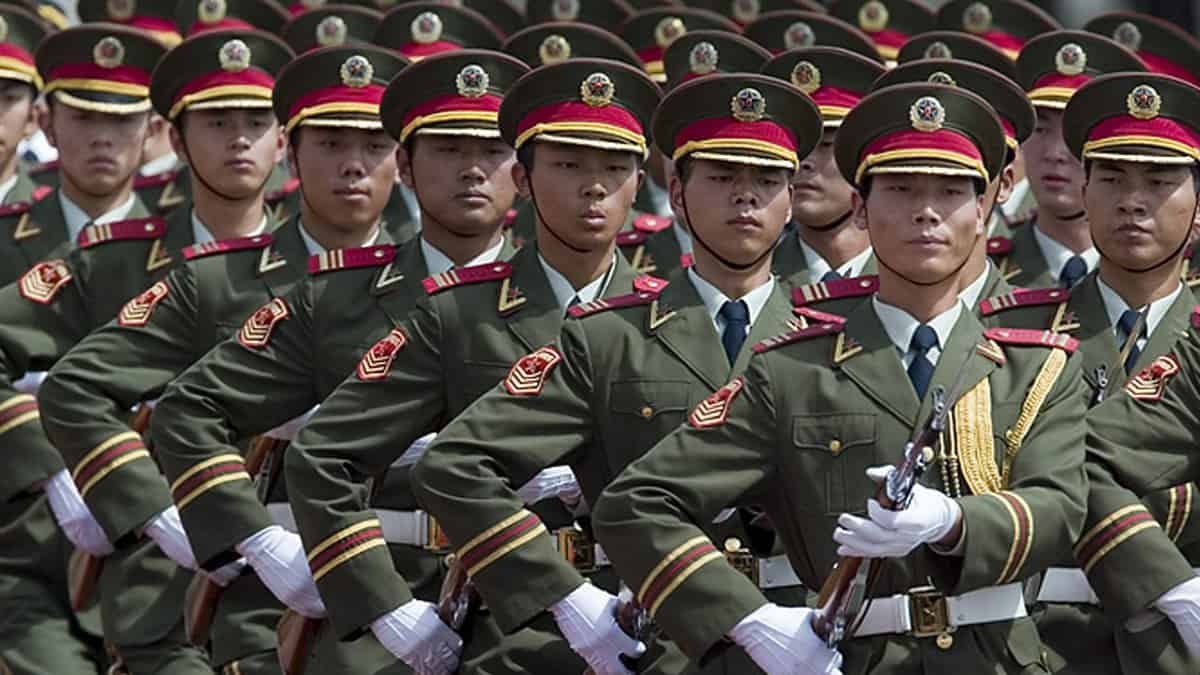 A row of soldiers marching with guns in ceremonial uniforms. 