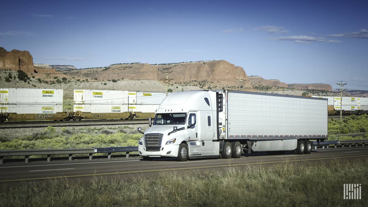 A photograph of a truck. Intermodal containers are behind the truck.