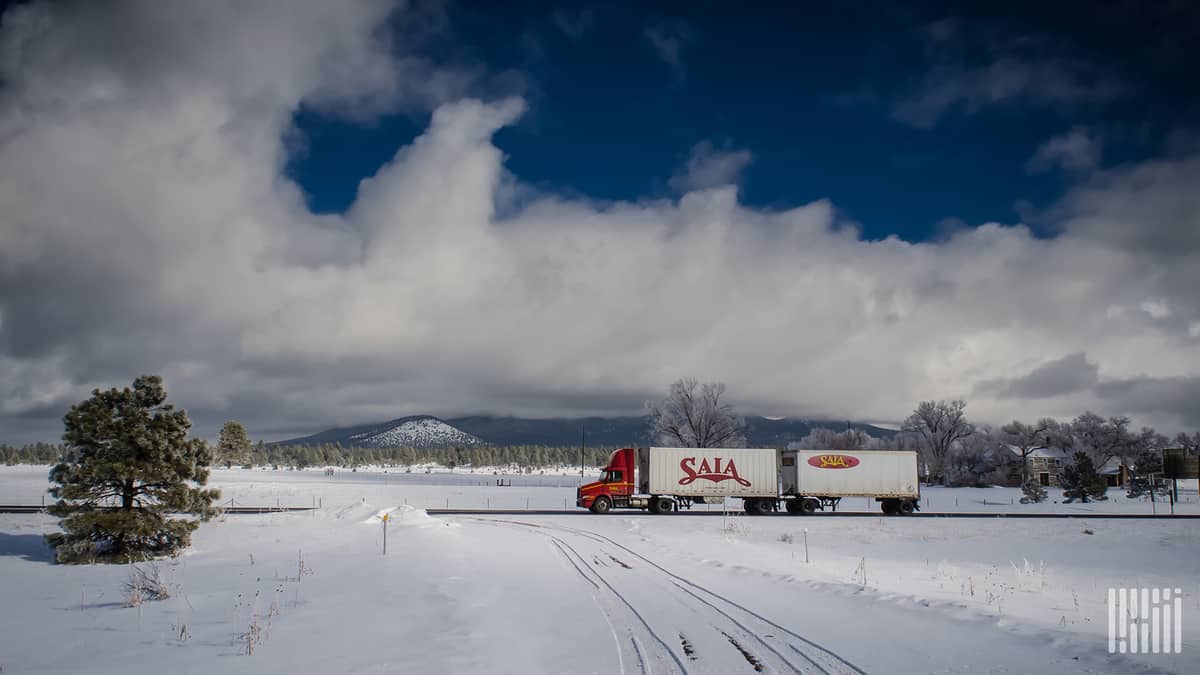 Tractor-trailer moving through snowy area.