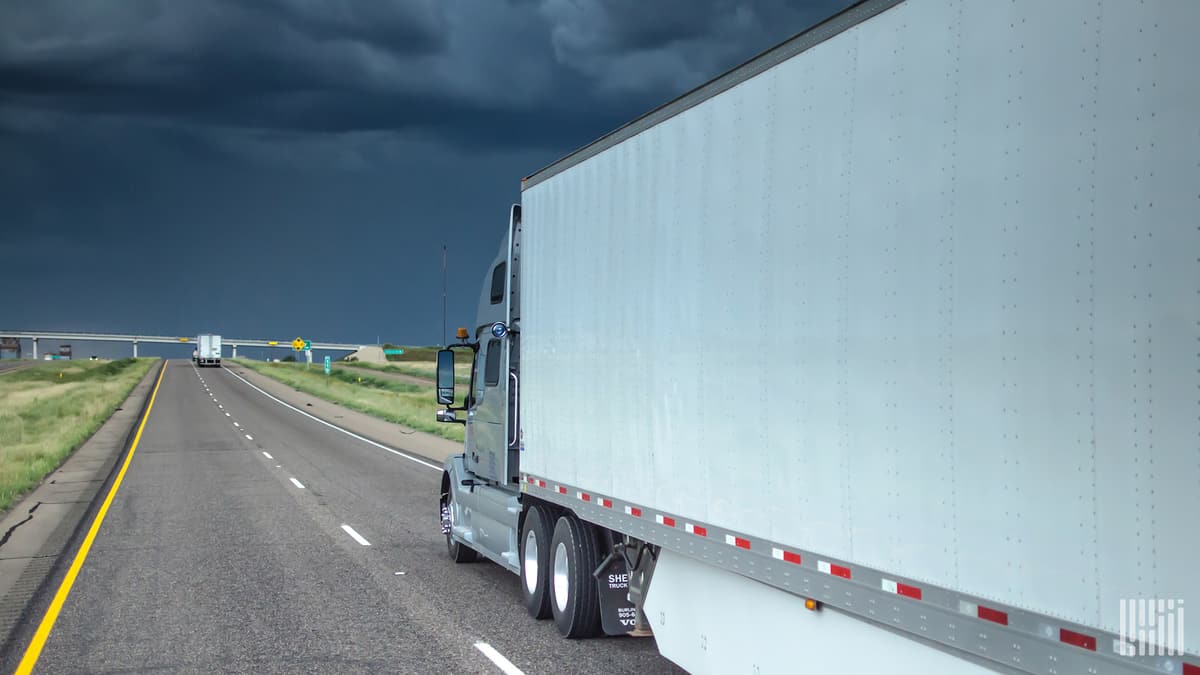 Tractor-trailer heading toward cloudy, dark skies.