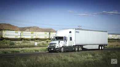 White truck with double-stack intermodal train in background
