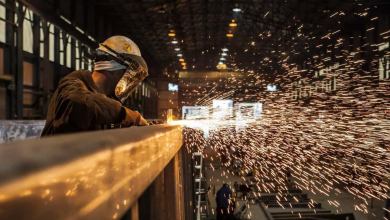 A photograph of a worker melding equipment. Sparks of fire are coming from the equipment.