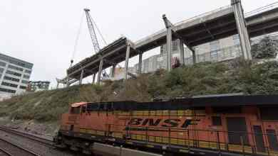A photograph of a train locomotive traveling next to a construction site.