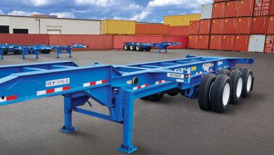A photograph of an intermodal chassis at a container yard. There are intermodal containers stacked in rows behind the chassis.