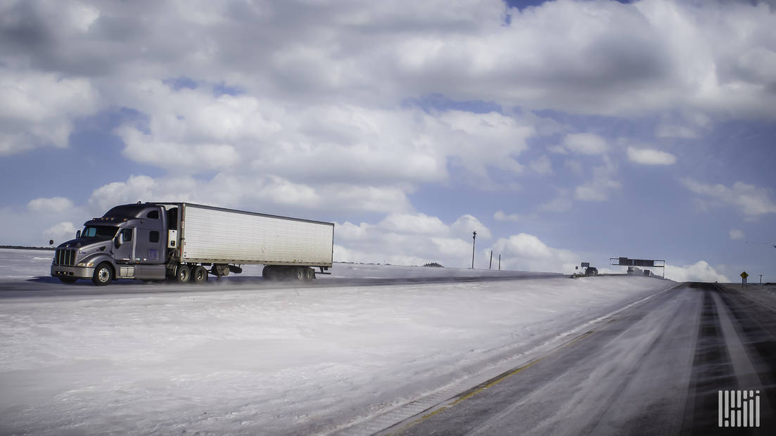 Tractor-trailer heading down snow-covered highway.