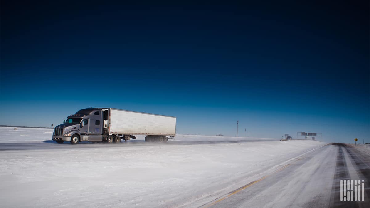 Tractor-trailer heading down a snowy road.