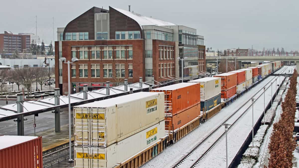 A photograph of a train hauling intermodal containers traveling through a downtown area in wintertime.
