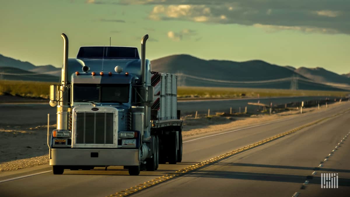 Flatbed truck hauling a load on the highway with hills in the background.