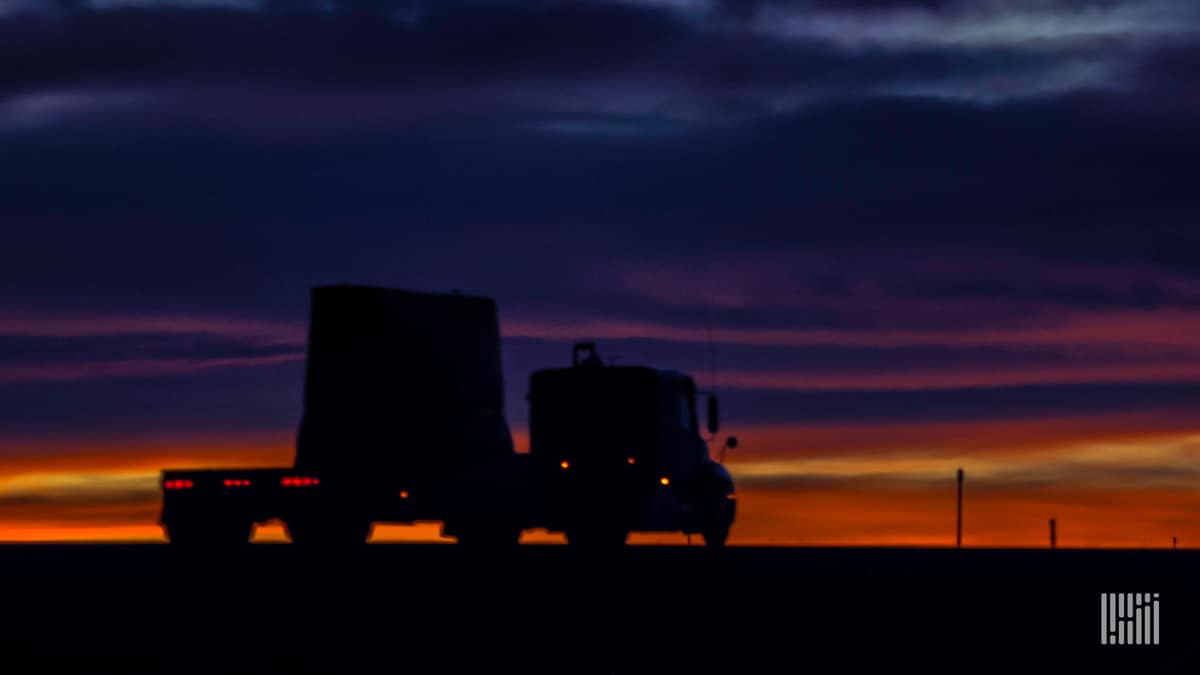 Flatbed truck on highway at sunset.