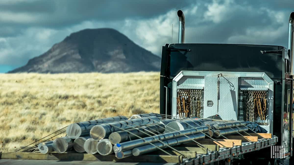 Flatbed truck carrying pipe with thunderstorms in the distance.