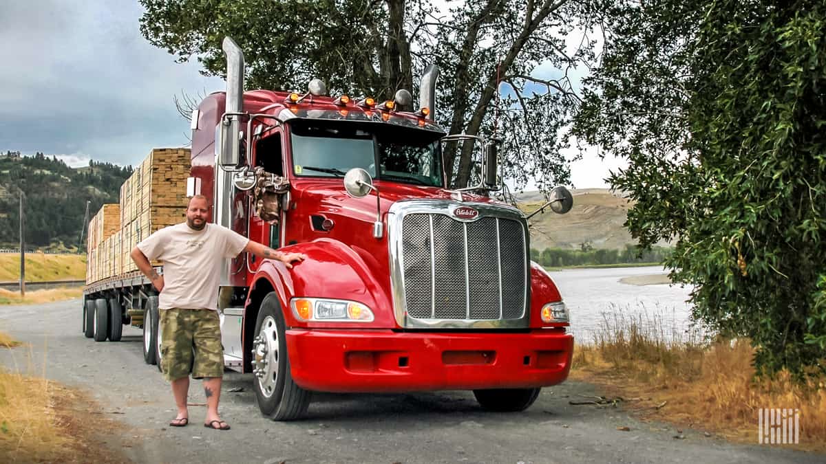 driver standing next to his tractor with flatbed of lumber