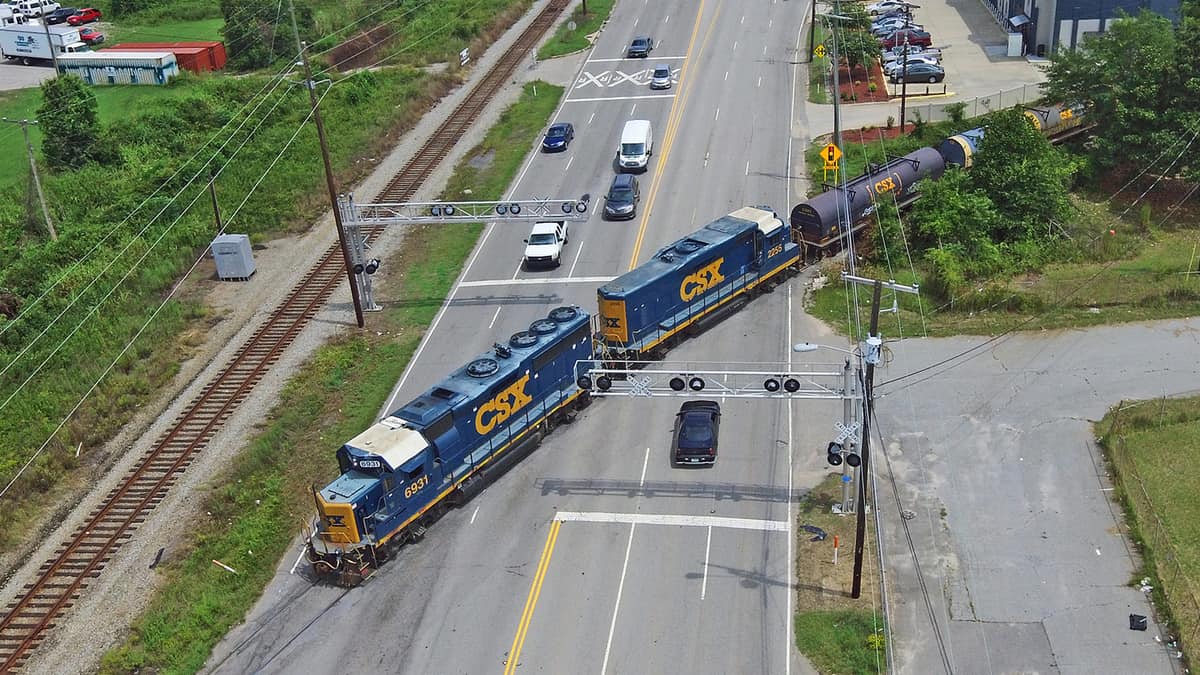 An aerial photograph of a train driving through a road. Vehicles on either side of the train are waiting for the train to pass by.