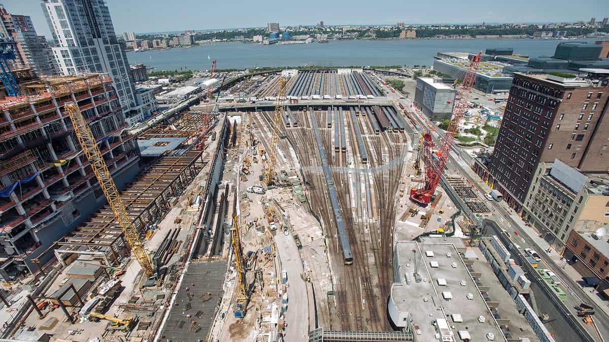 A photograph of a rail yard in construction. The yard is in a city next to a river.