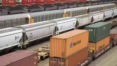 A photograph of different types of railcars sitting on rail tracks at a rail yard.