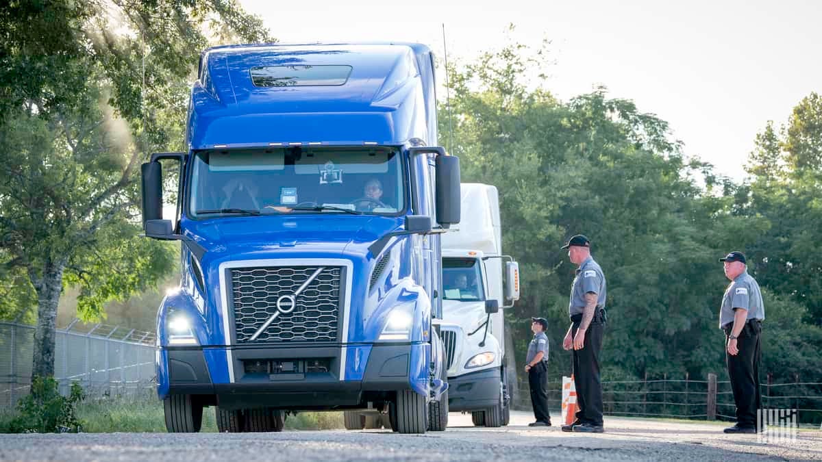 Trucks in line to deliver supplies. There are public safety officers standing to the side of each truck.