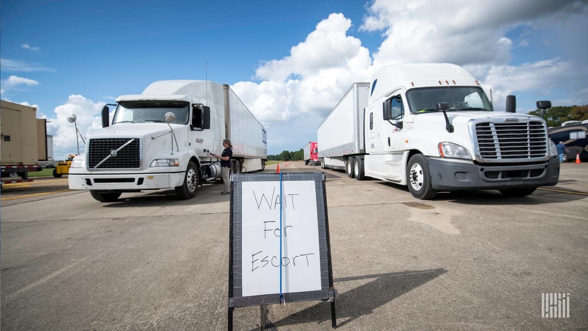 Trucks lined up ready to deliver supplies. Sign says: "Wait for Escort."