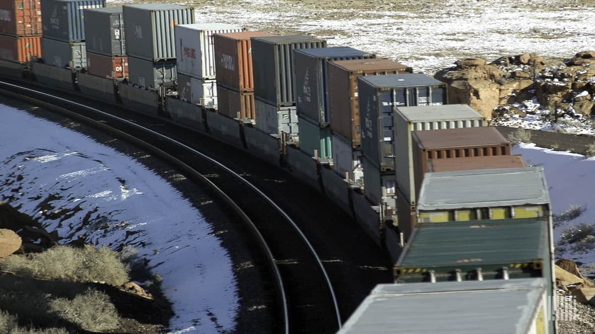 A photograph of a train hauling intermodal containers through a snowy field.