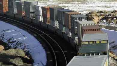 A photograph of a train hauling intermodal containers through a snowy field.