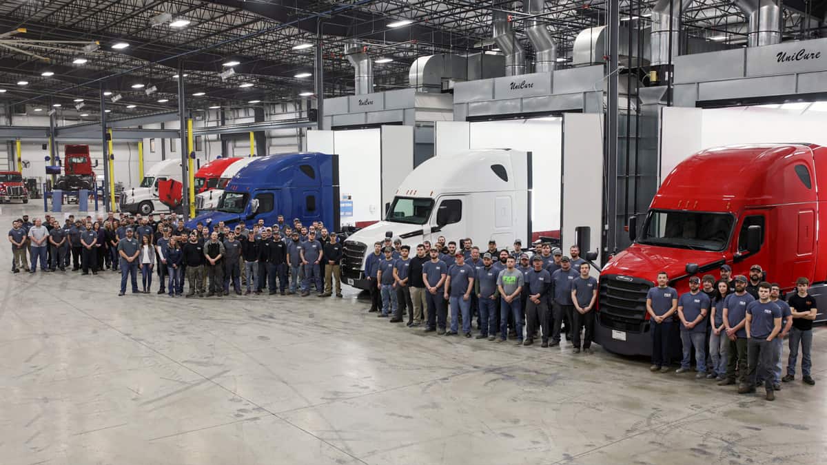 Group of truck repair workers gathered in front of red, blue and white trucks