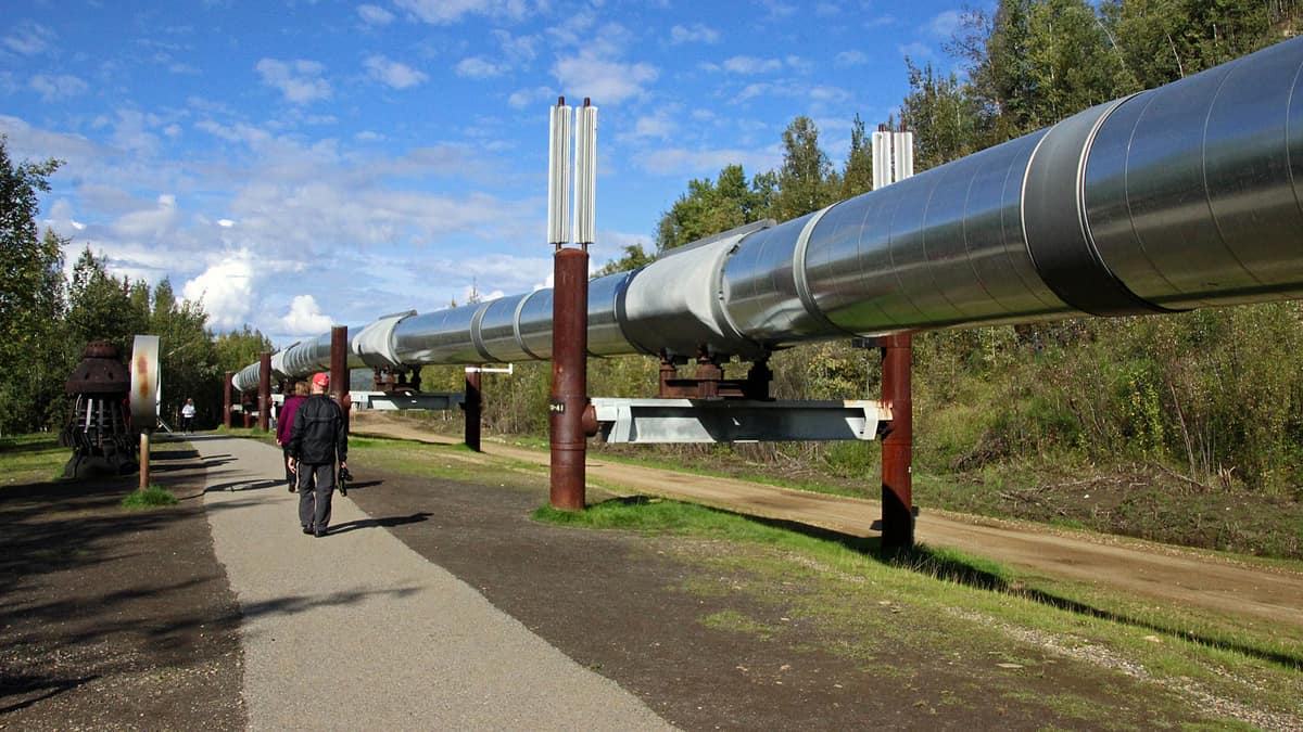 Part of the Trans-Alaska pipeline system (above-ground) with workers walking by it. 