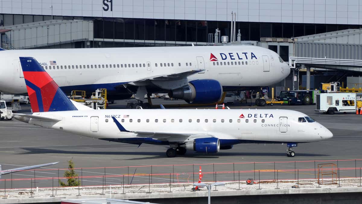 A big white Delta jet next to a smaller one at airport.