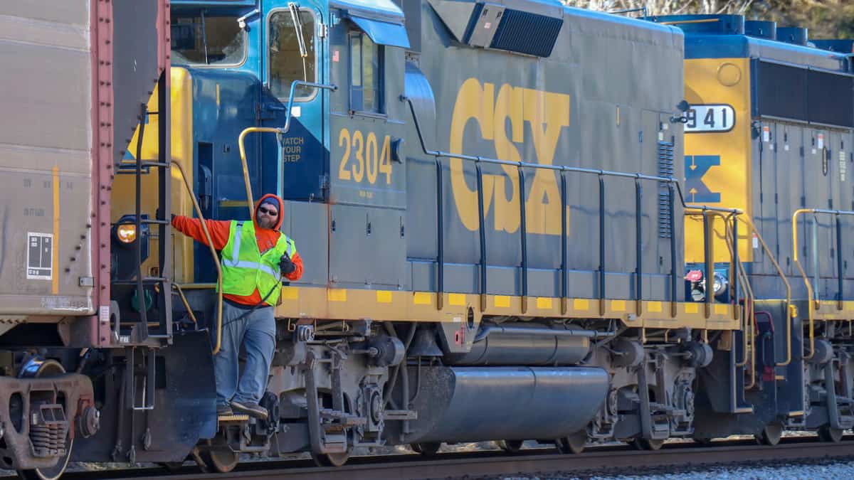 A CSX employee stands on the stairs of a CSX locomotive.