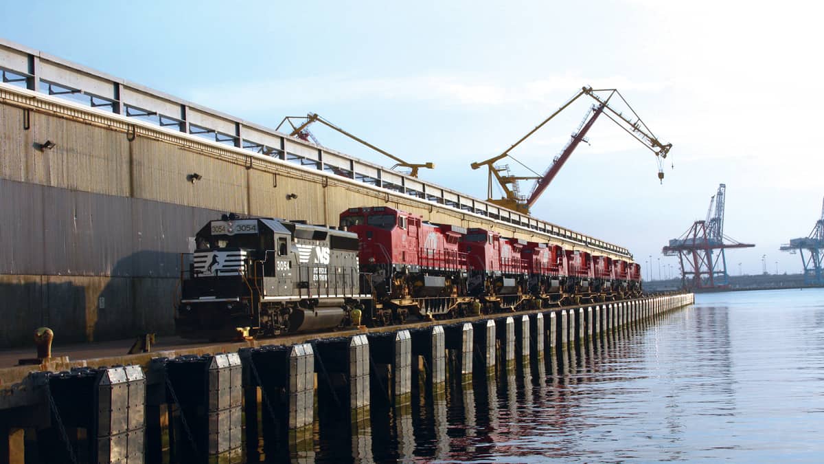 A photograph of a train on the dock of a port. The train is next to the water.