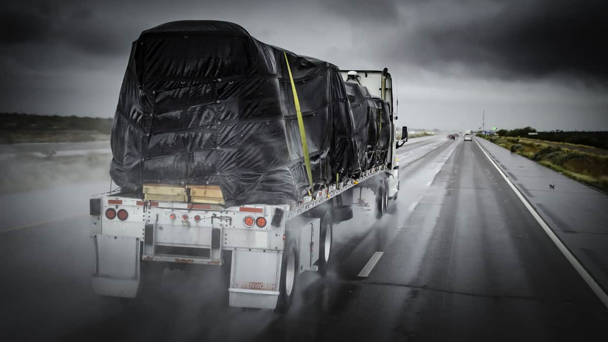 Covered flatbed tractor-trailer on wet highway.