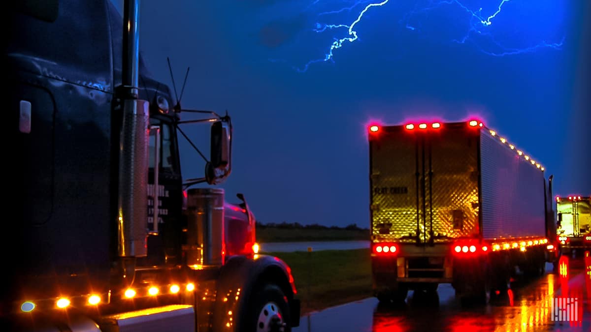 Tractor-trailers going down highway with lightning in the sky ahead.