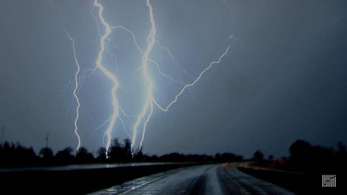 Lightning in the sky, tractor-trailers in the distance on a highway.