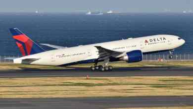 A big white Delta plane lifts off from runway.