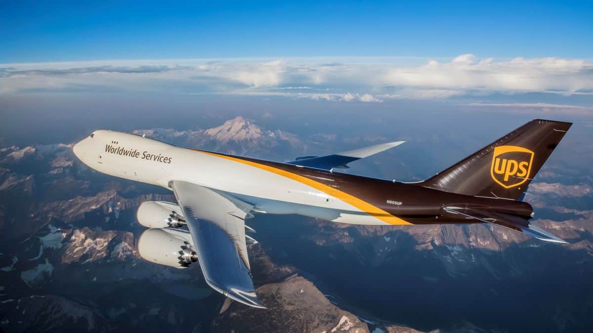 UJPS brown and white jumbo jet flies over mountains.