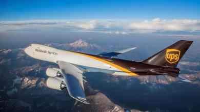 UJPS brown and white jumbo jet flies over mountains.