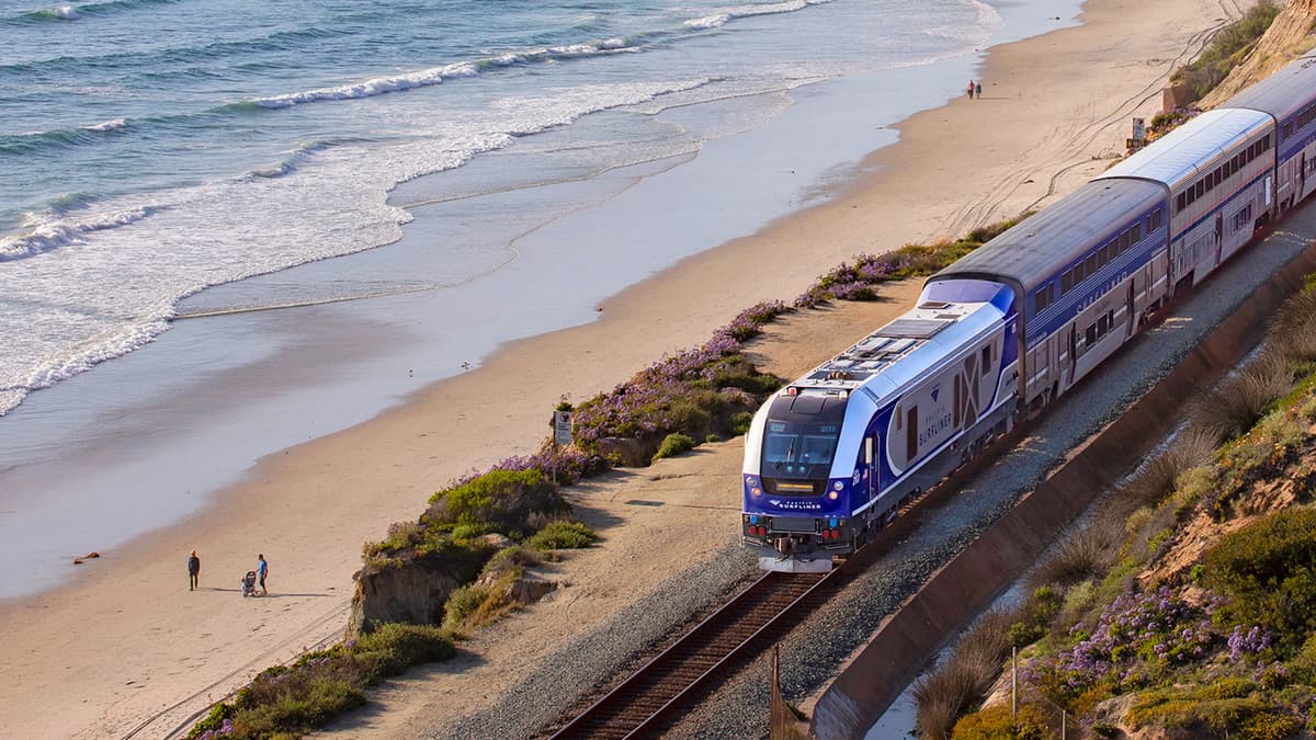 A photograph of a train traveling by a beach.