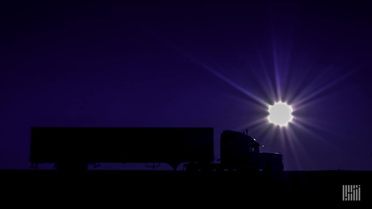 Sun jut above the horizon at dusk, with tractor-trailer in the foreground.