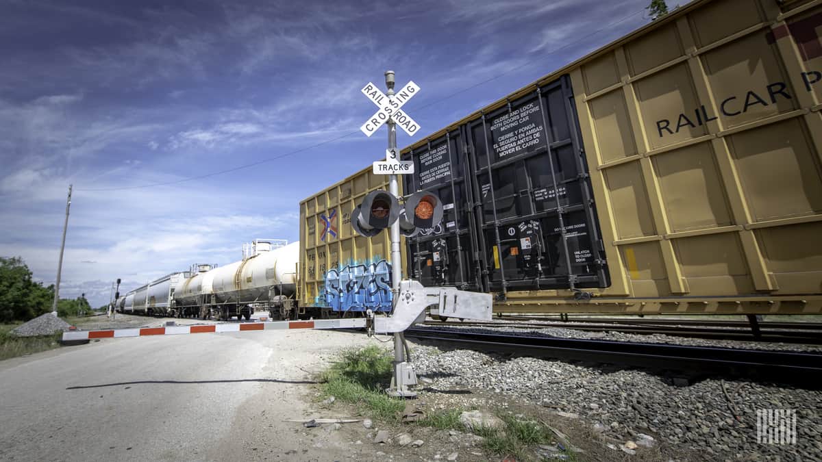 A photograph of boxcars and tank cars at a rail crossing.