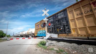 A photograph of boxcars and tank cars at a rail crossing.