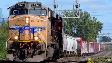 A photograph of a train locomotive pulling railcars on a sunny day.