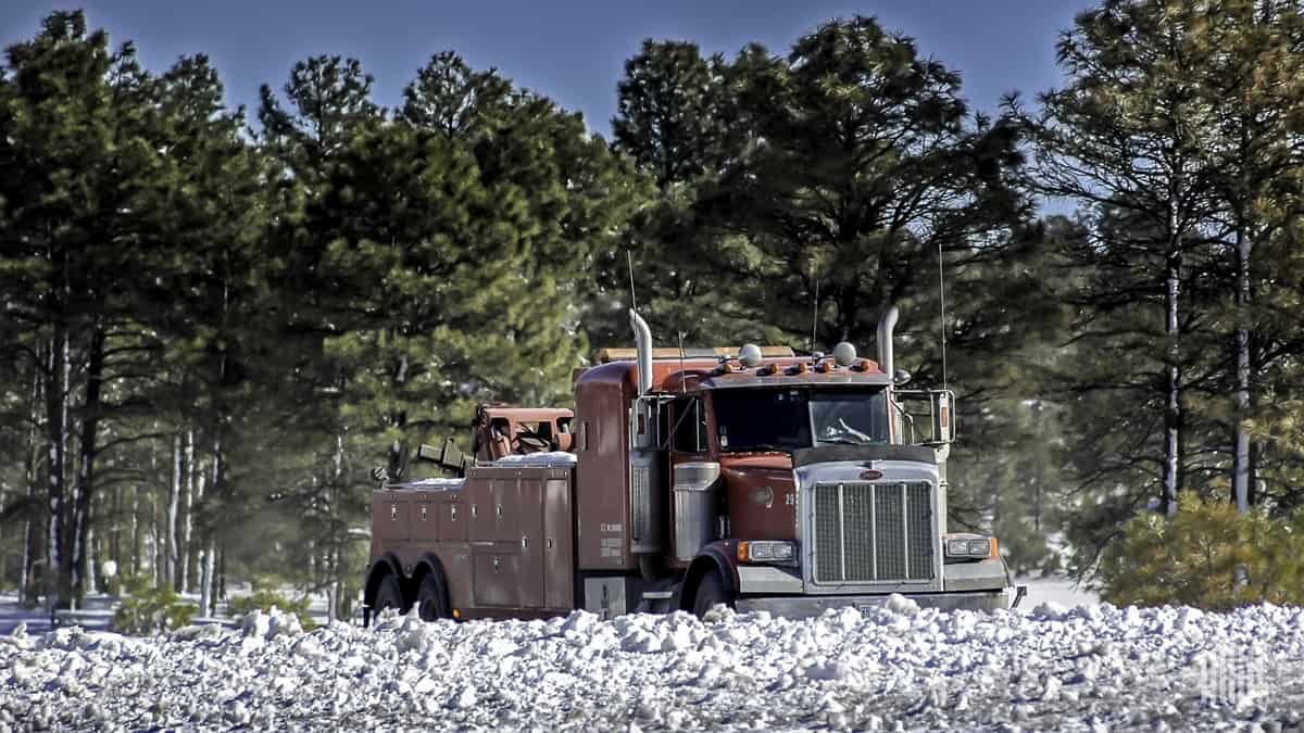 Flatbed truck on road with snow-covered hillside.