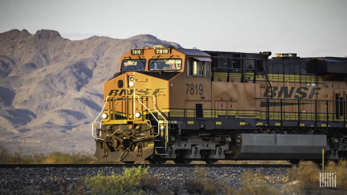 A photograph of a freight train locomotive. In the background is a mountain range in the desert.