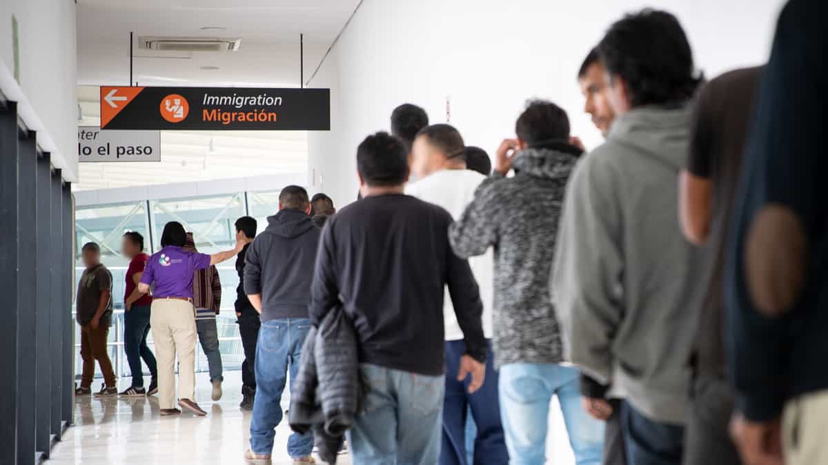 A photograph of people waiting in a long line inside a hallway.