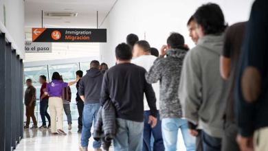 A photograph of people waiting in a long line inside a hallway.