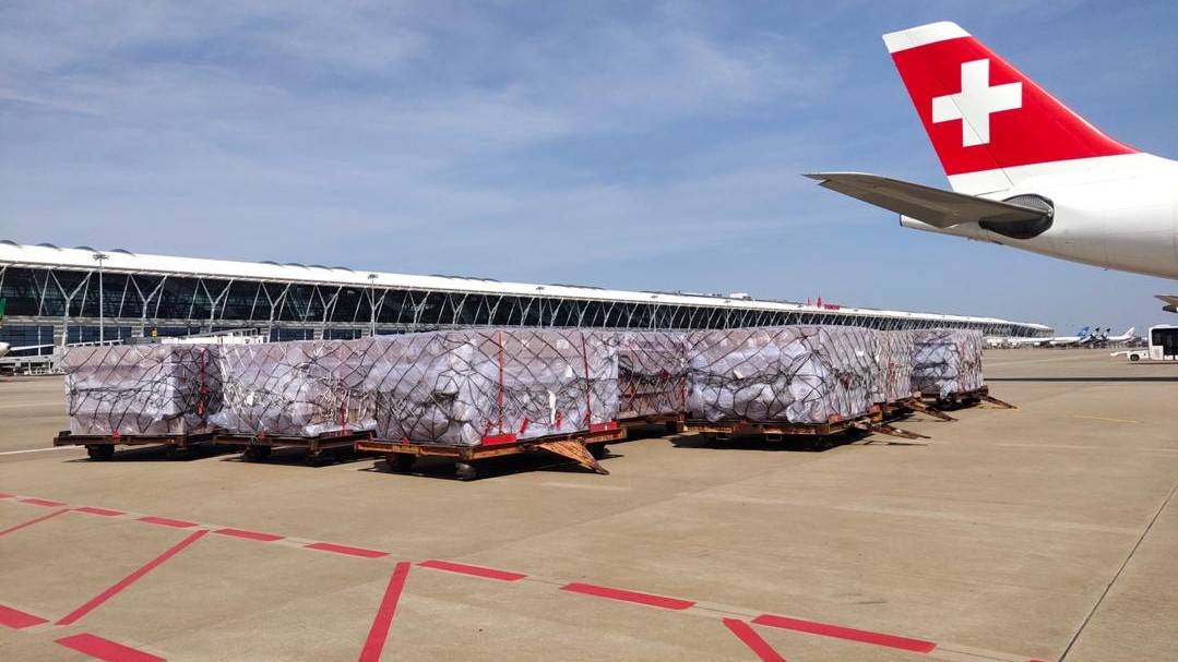 Cargo pallets on the tarmac and the tail of Swiss Air Lines with white cross on it